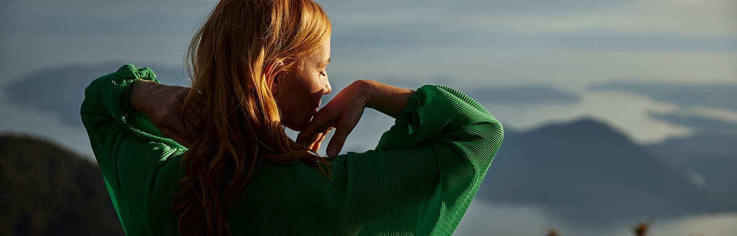 A woman in a green shirt stretches while looking down upon a valley.