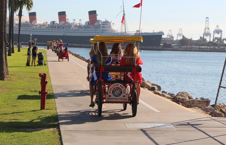 A group of individuals riding a covered four-wheeled bike along a seaside bike path.