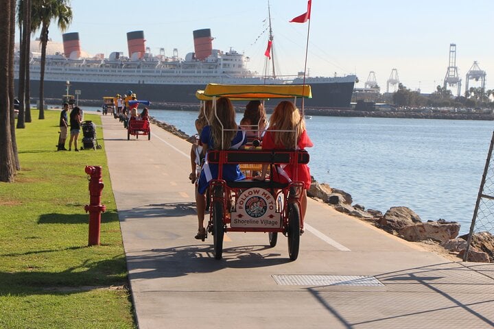 A group of individuals riding a covered four-wheeled bike along a seaside bike path.
