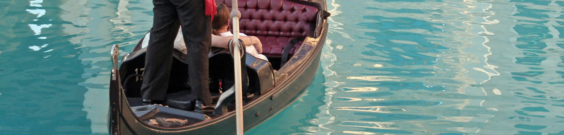 A gondolier pushes a gondola along a waterway, a couple in the seat for the ride.