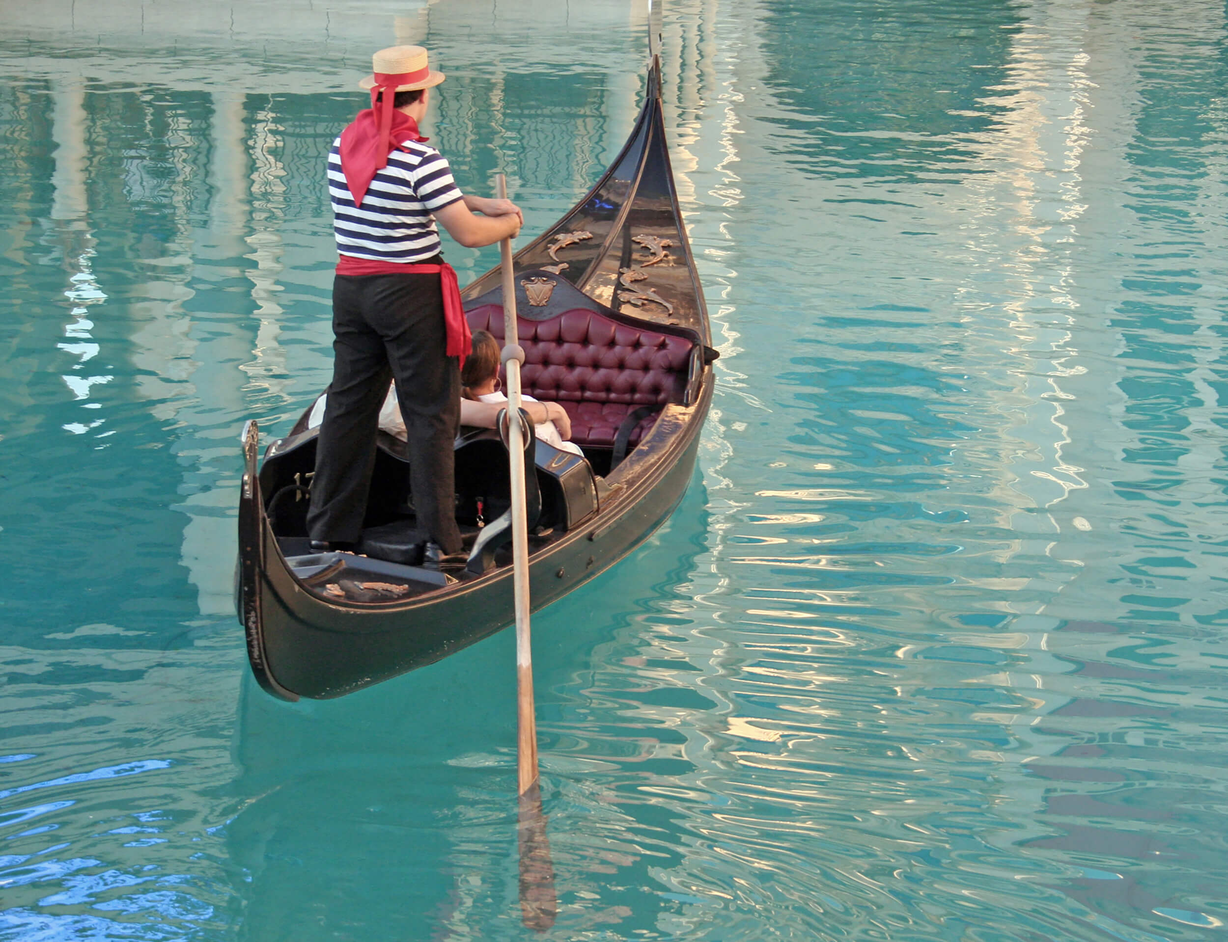 A gondolier pushes a gondola along a waterway, a couple in the seat for the ride.