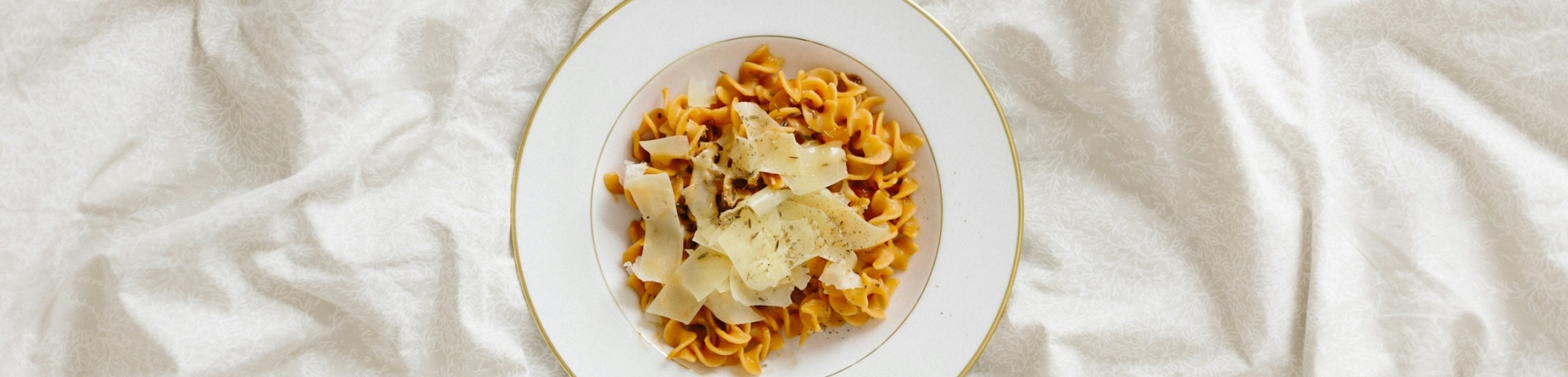 A pasta dish with lots of parmesan cheese on a white, papery backdrop.