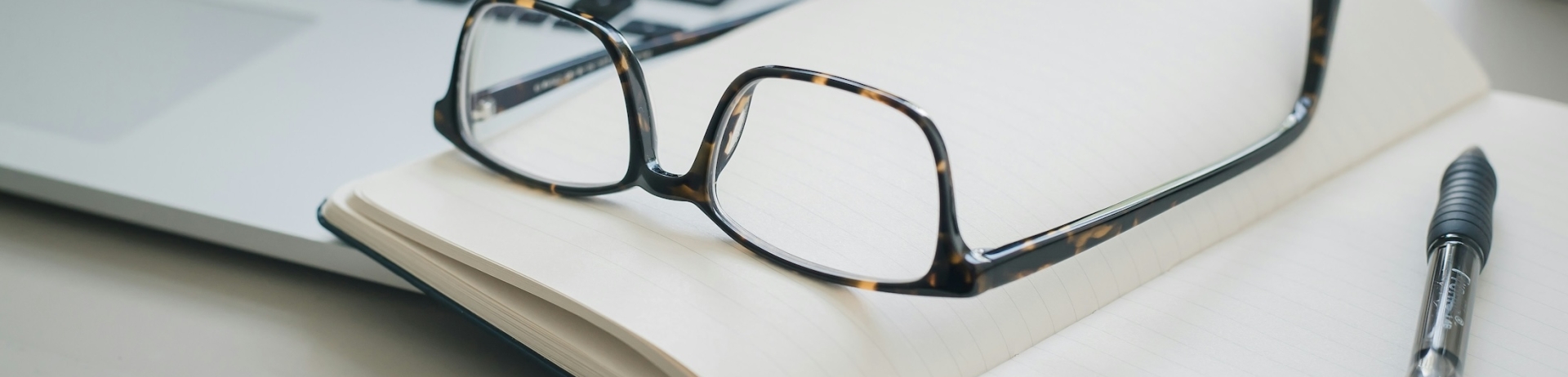 Glasses balanced on a notebook next to a MacBook laptop.