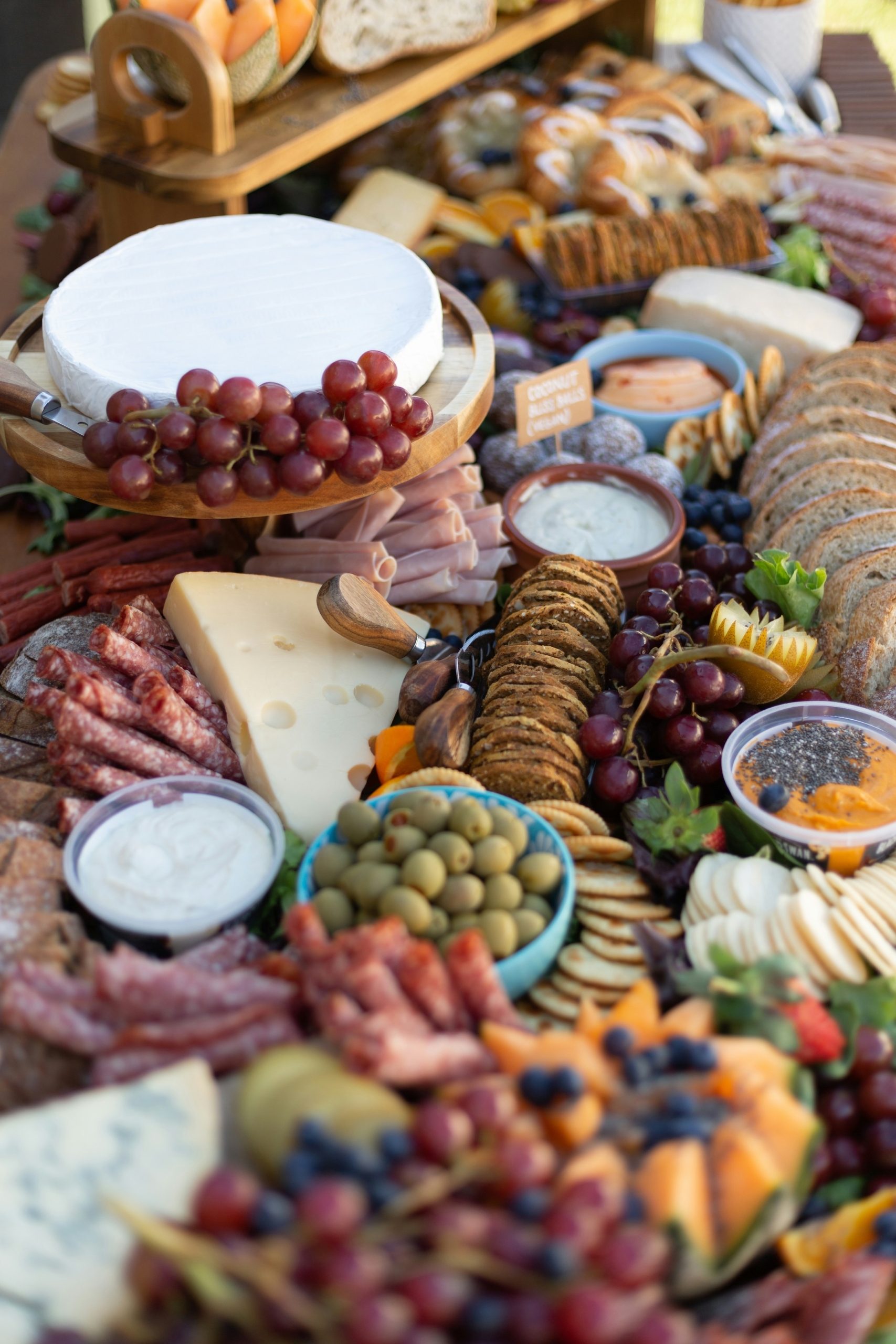 An intricate charcuterie board with assorted soft and hard cheeses, crackers, grapes, melon, olives, dips, cured meats.