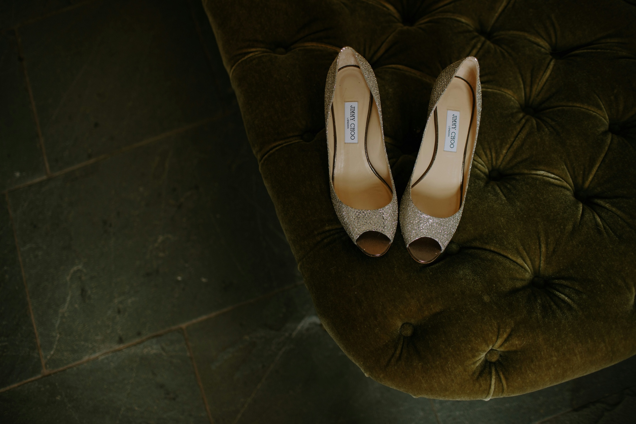 A pair of silver sparkling Jimmy Choo high heel shoes on a green velvet cushion.